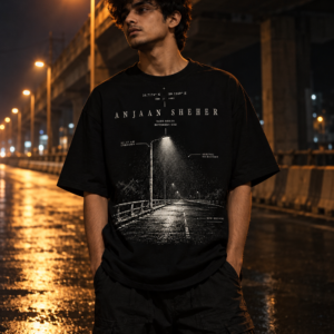 Young man wearing a black oversized t-shirt with Anjaan Sheher graphic text on a wet city street at night