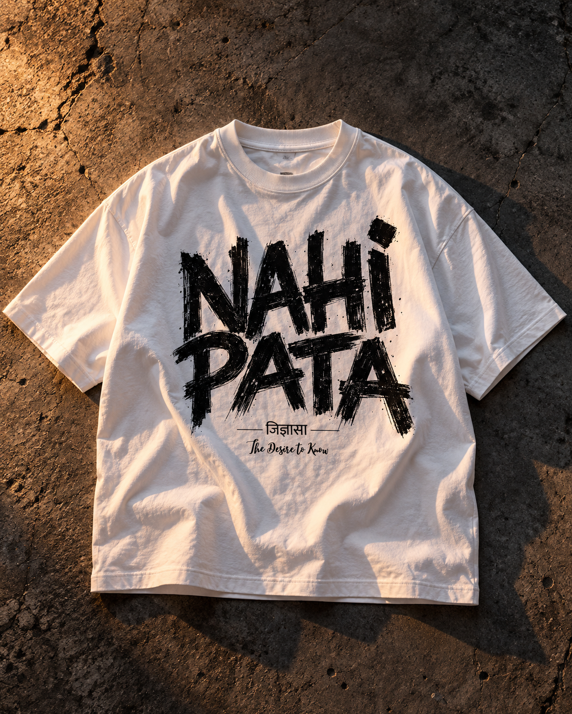 Flat lay of a white Nahi Pata oversized tee on grey concrete showing full-chest lettering and ribbed collar