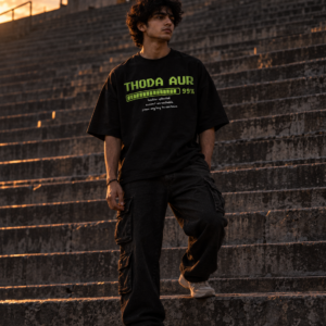 Man in a black Thoda Aur oversized tee standing on long concrete stadium steps at dusk